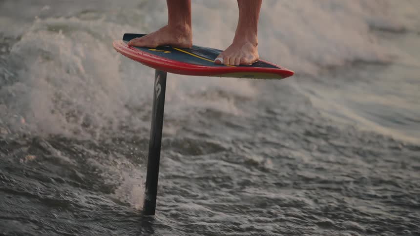 Bare feet balance on a hydrofoil board as it glides above the choppy water