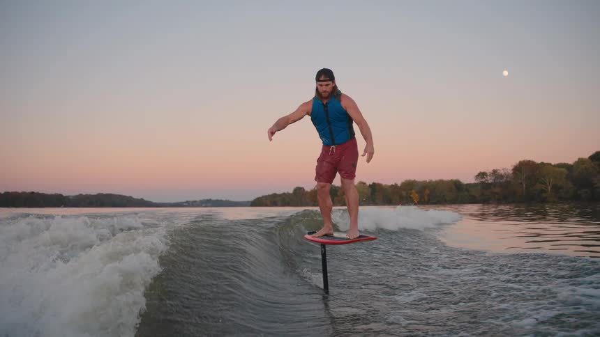 A man rides a hydrofoil board on a lake at sunset
