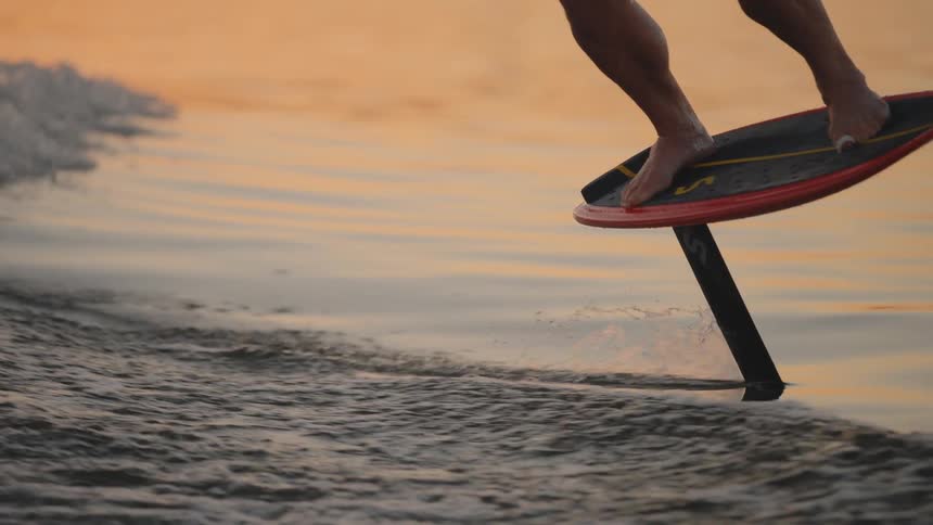 A person surfs the ocean at midday standing on a surfboard and riding along with the waves