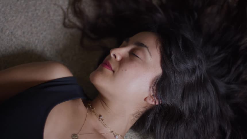 Lying on the carpet a woman with closed eyes shows a calm expression