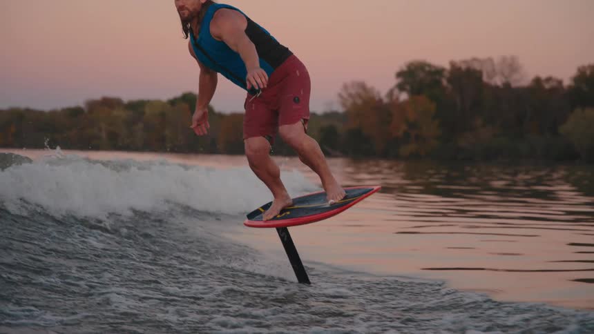 A young man rides a surfboard in the ocean at midday gliding smoothly through the waves with the shoreline visible in the distance