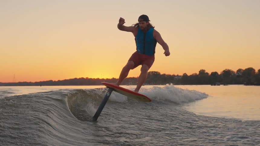A man rides a hydrofoil board on a lake at warm golden sunset