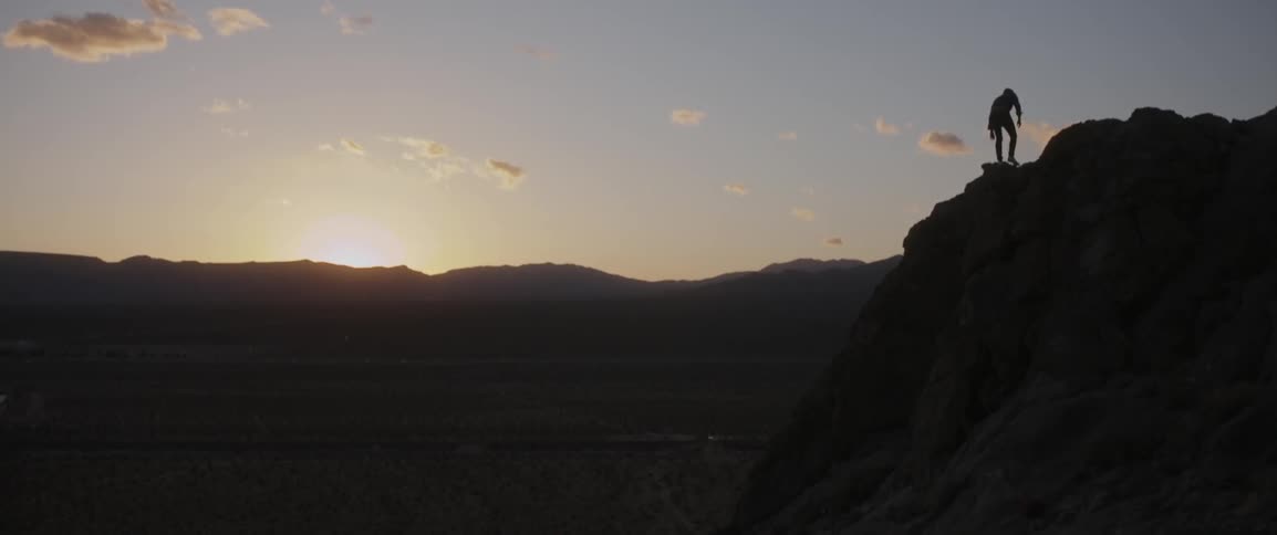 Person climbs up a cliff at sunset