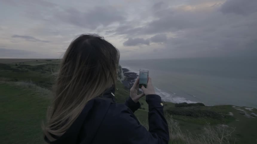 A woman takes a photo with her phone near the shore