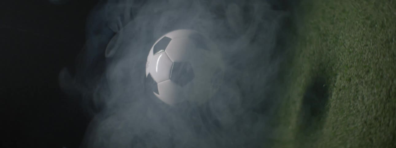 Soccer ball suspended in air surrounded by thick smoke above partially visible grass