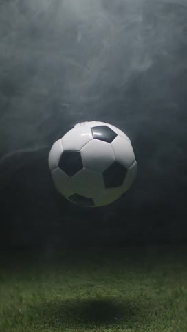A soccer ball is suspended in the air above grass and surrounded by smoke