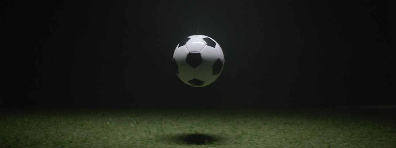 Soccer ball suspended above grass with shadow cast on dark background