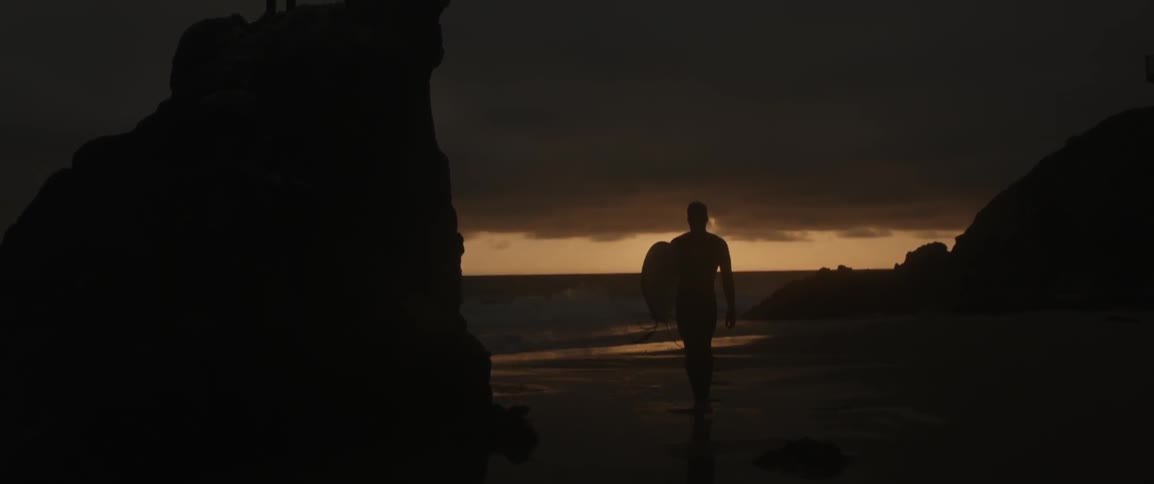 Man holding surfboard walking away from ocean after sunset
