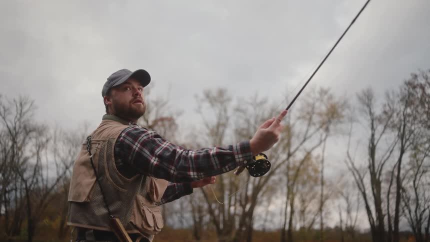 Person fly fishing in a leafless tree setting under a cloudy sky