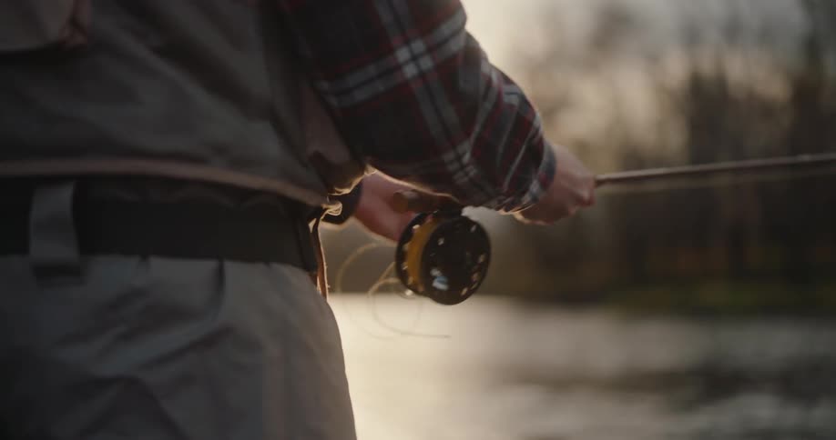 Close up of a man releasing a fishing line into a flowing river outdoors at sunset