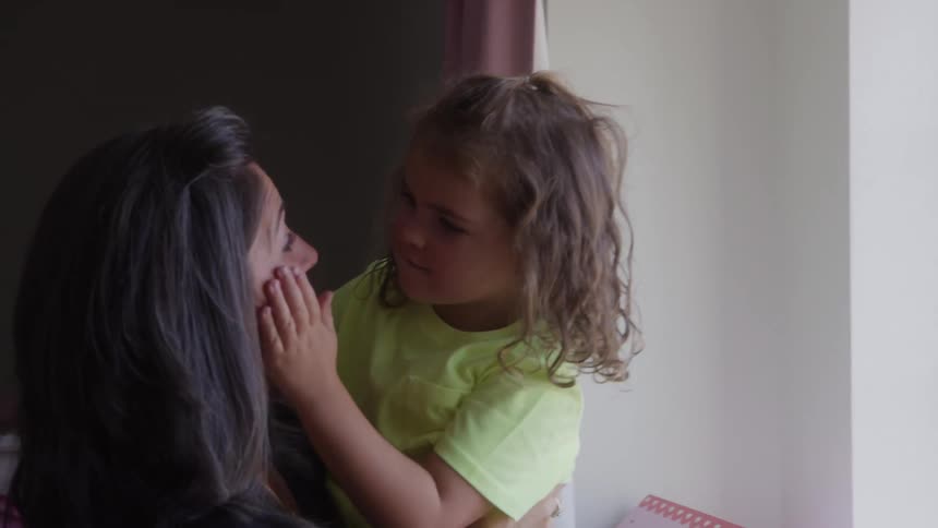 Mother points at something outside the window while holding her daughter