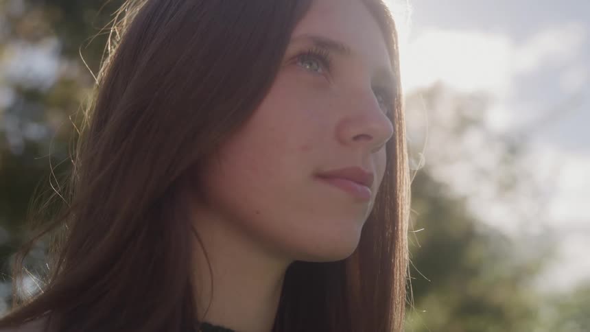 The video features a closeup shot of a young womans profile with her long dark hair framing her face as she looks up and slightly away from the camerashe is heavily backlit by the sun creating a strong lens flare and a cinematic warm glow around