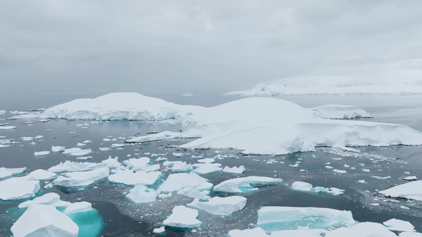 Aerial view of icy waters and snow covered land under a grey sky