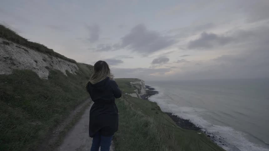 A woman stands in the wind watching the shore