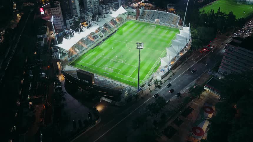 Highway traffic and a train pass a soccer game being played in a brightly lit stadium at night