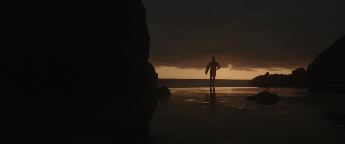 A surfer runs on a beach at sunset