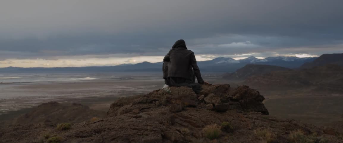 A person sits on a pile of rocks overlooking a valley