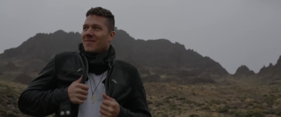 A man adjusts his leather jacket outside on an overcast day