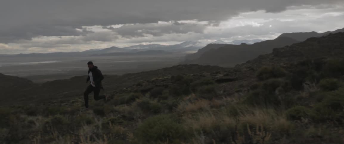 Man running through shrubbery in desolate mountain area