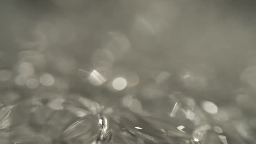 This is a very closeup abstract macro shot of liquid boiling showing large rapidly forming and breaking bubbles the video is monochromatic or grayscale with sparkling highlights and a shallow depth of field dissolving into an outoffocus bokeh ba