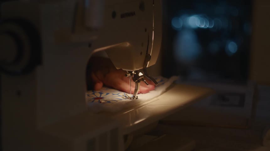 Female hands sewing a patterned cloth on a machine indoors during night time