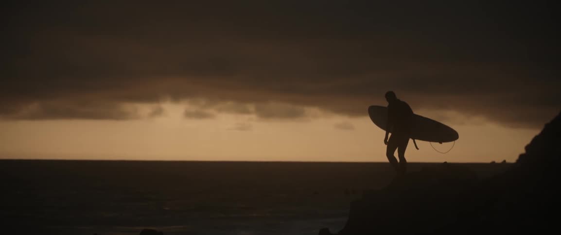 A surfer stands on a beach at sunset
