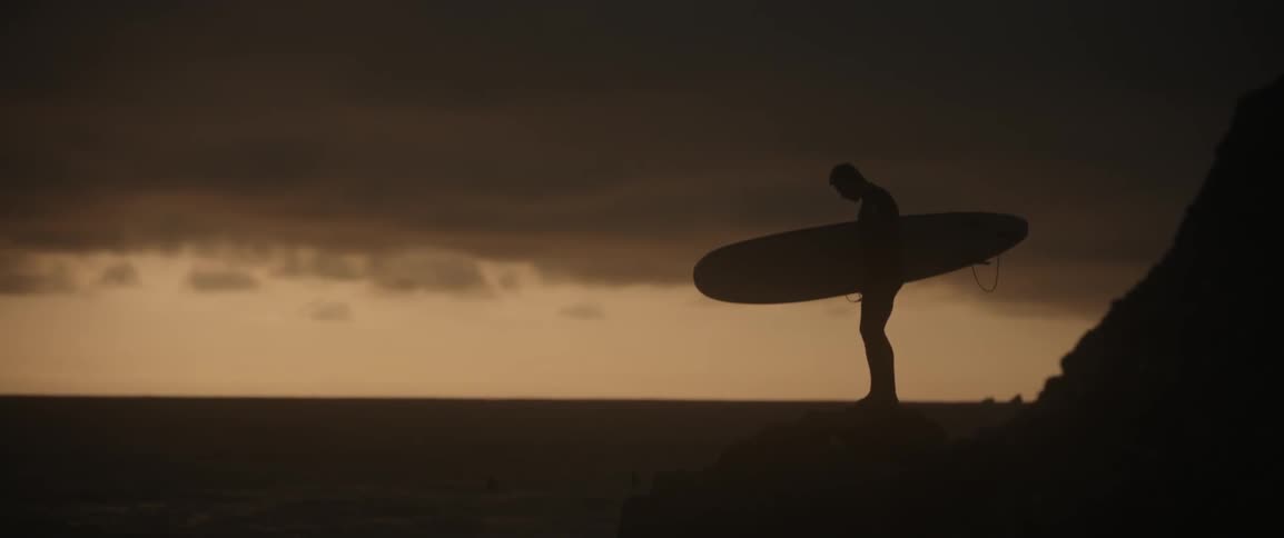 A surfer stands on a beach at sunset