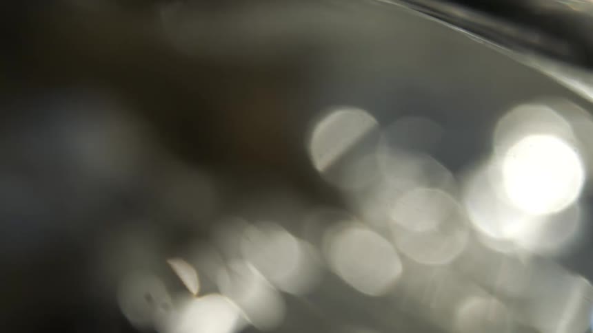 The video is an abstract visual sequence dominated by dark and bright contrasts featuring large outoffocus bokeh circles that are mostly white and grayinterspersed with the soft bokeh are moments of sharp bright light reflections and refractions
