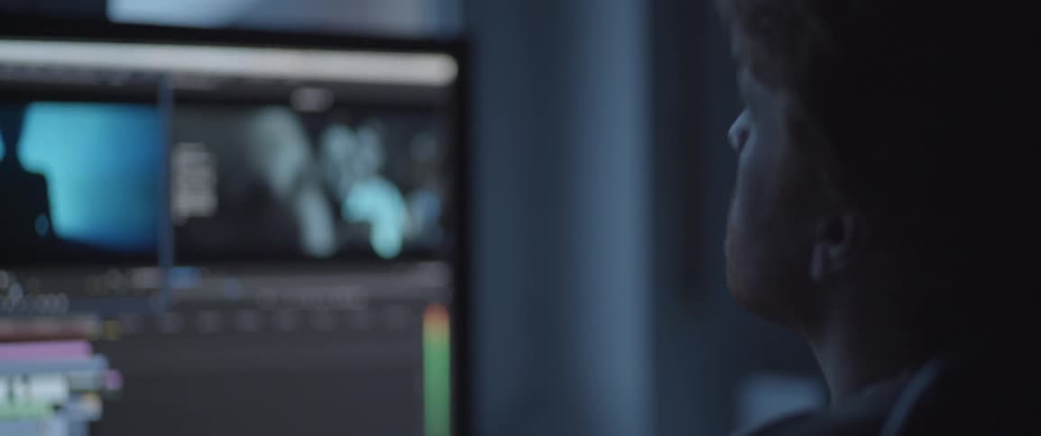 A man sits in a dark room looking at monitors