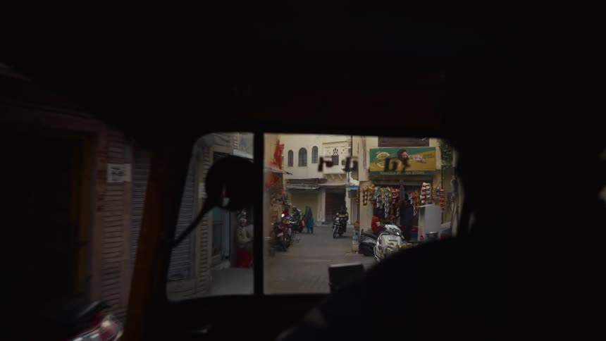 Narrow street seen from inside a vehicle shows movement with motorcycles and pedestrians