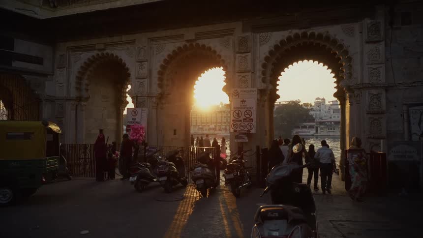 Ornate arched entrance lit by the setting sun with people and vehicles moving through the area