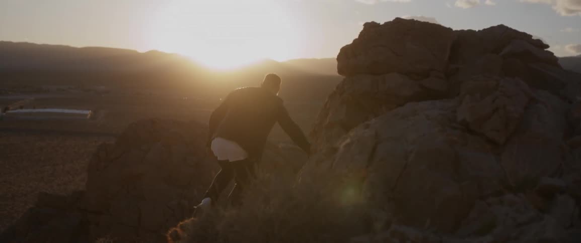 A man is climbing over some rocks at sunset