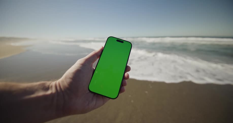 Hand holds a phone at the beach in front of the waves