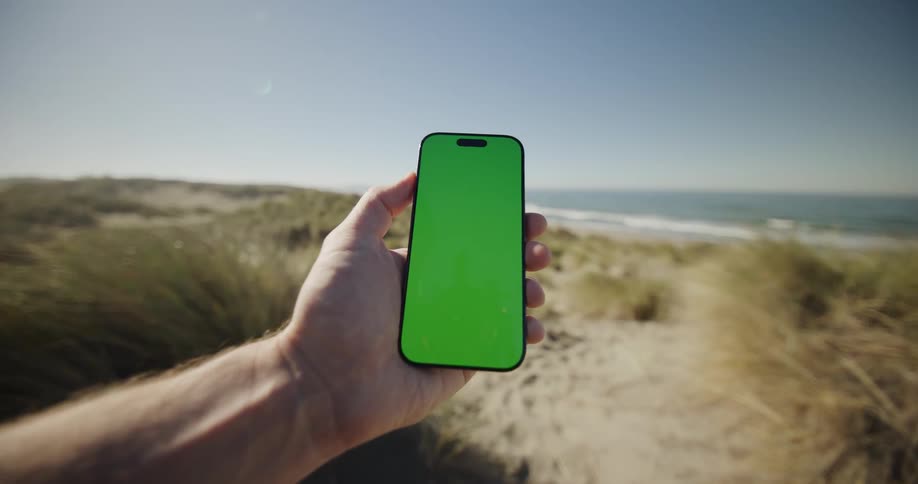 A man holds a smart phone and swipes up while standing at the coast