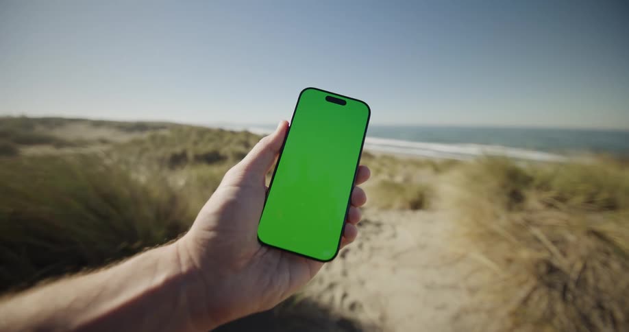 Hand with phone stands out against coastal dunes and clear blue sky