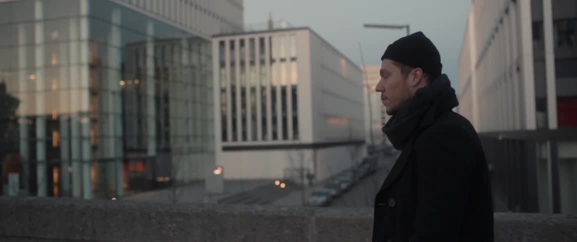 A man walks across a bridge by some buildings