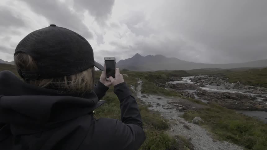 Woman taking photograph of mountains on cloudy day