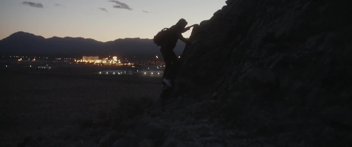 A man climbs up rocks at sunset