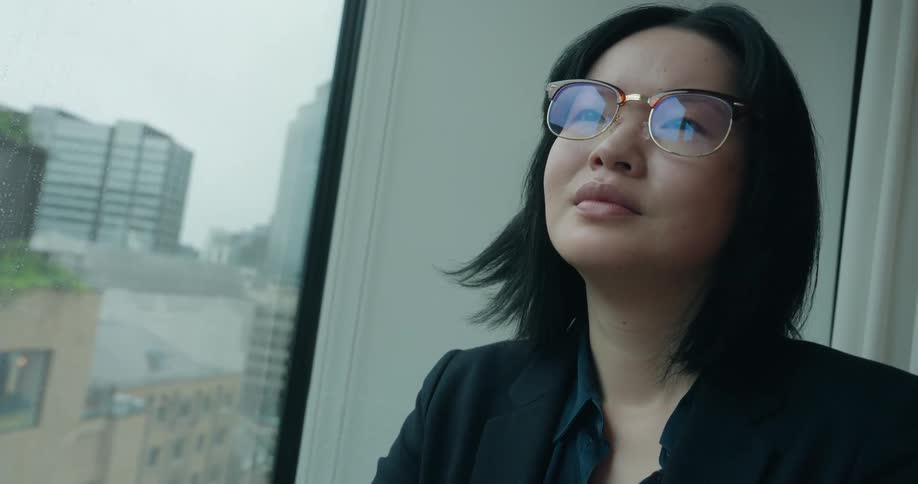 Woman leans against the window looking at the urban landscape on a cloudy day