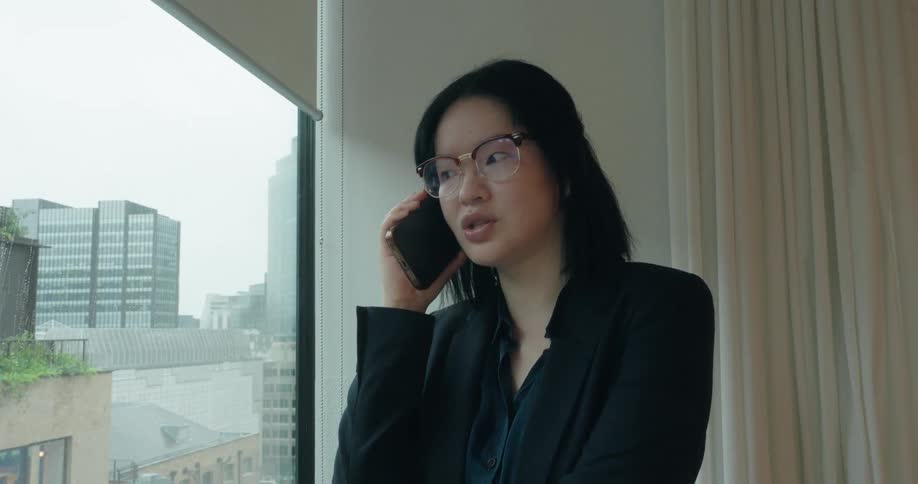 A woman talks on her phone while standing by a window in a modern office