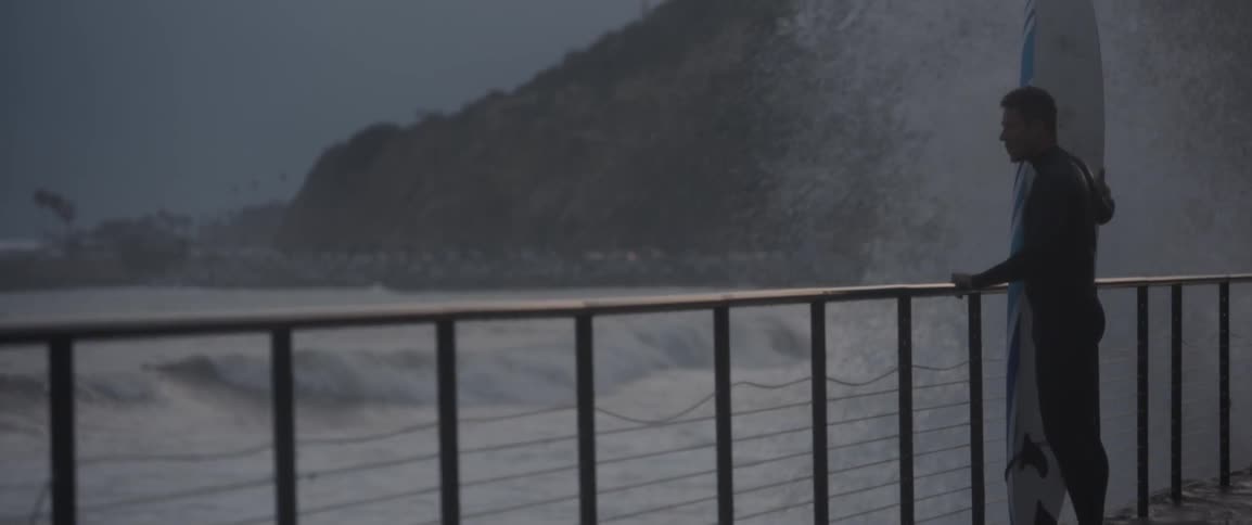 A man stands on a bridge being hit by waves