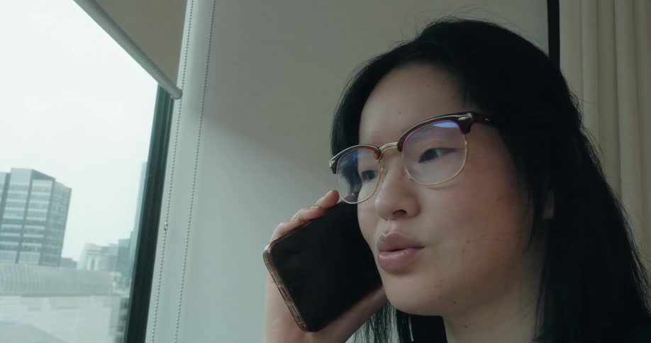 A woman is standing next to a window talking on her cellphone