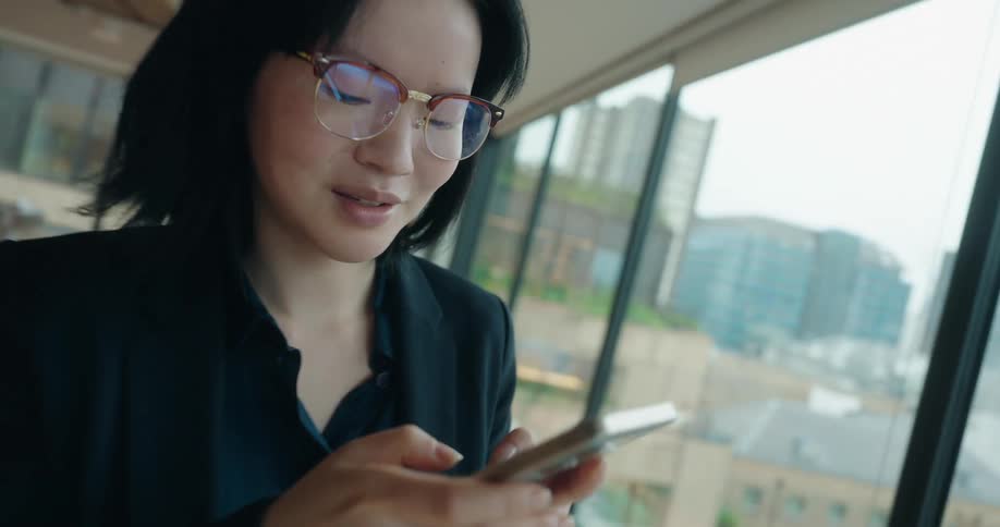A woman is standing near alarge window as she talks on her phone