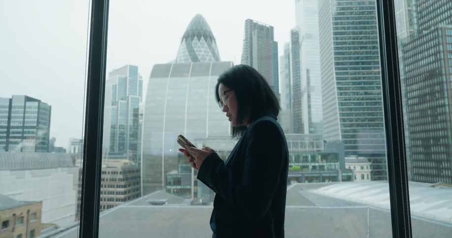 The woman is texting on her phone by the window