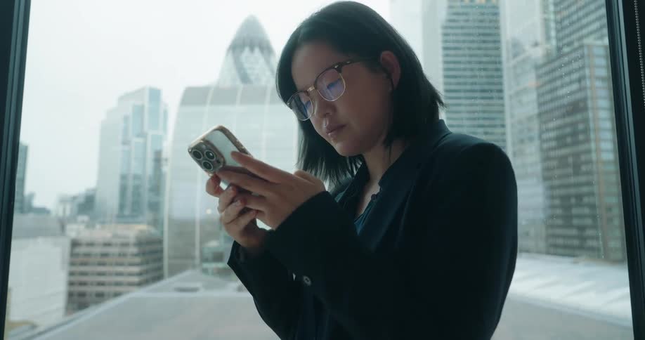 A woman uses her smart phone next to a window in an office building