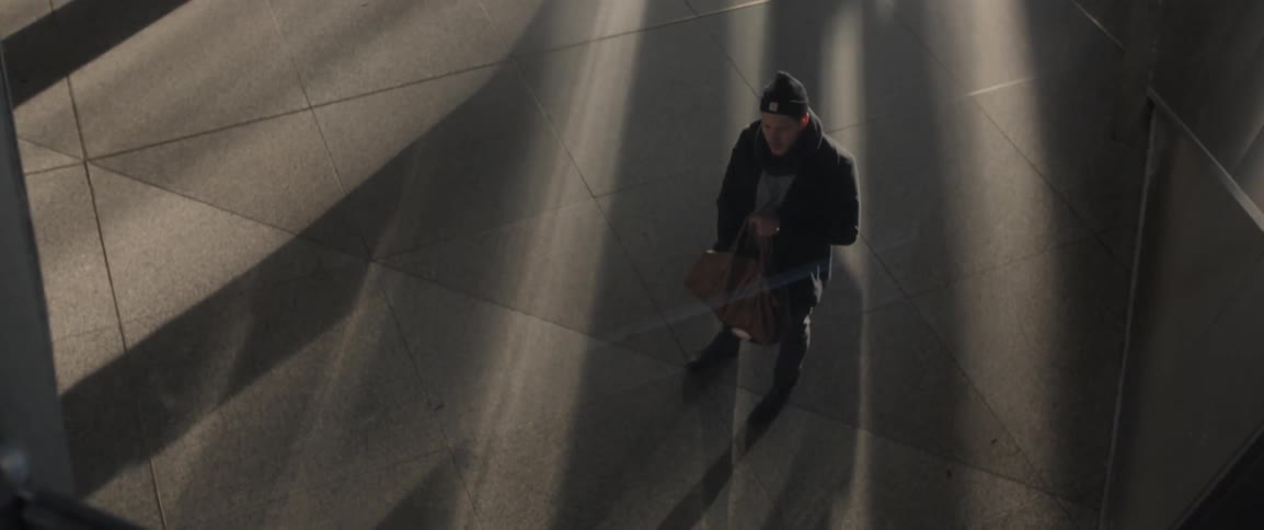 A man on a sidewalk at night holds a bag and starts to take something out of it as others walk by