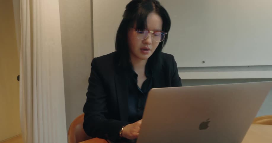 Woman sits at a table typing on a laptop computer