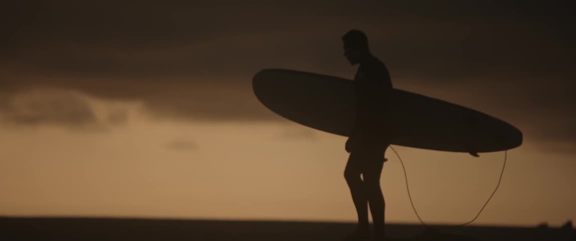 A surfer stands on a beach at sunset