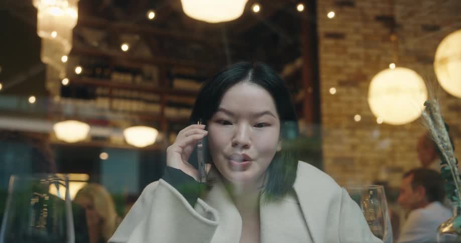 Woman talks on the phone while seated in a warmly lit restaurant
