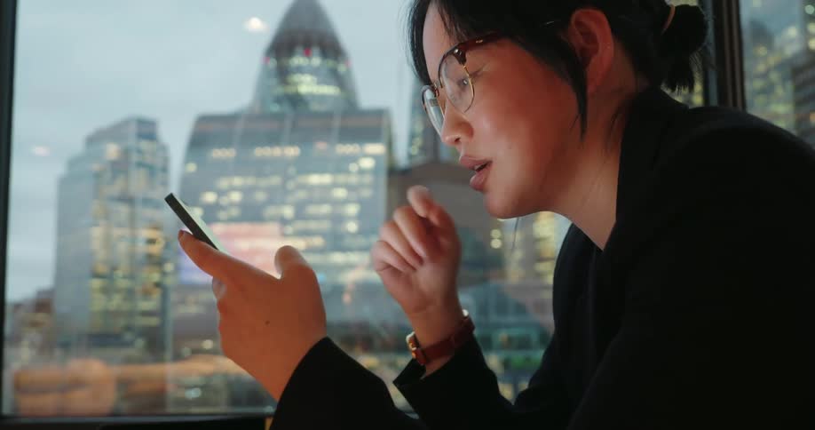 Woman sitting in the office in the evening texts on her smartphone